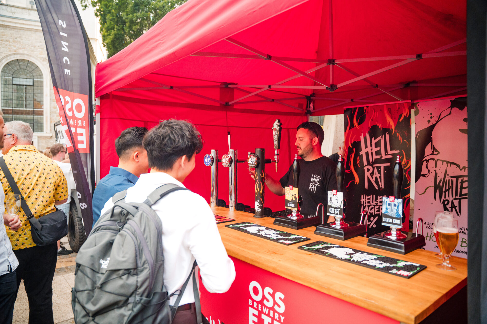 A person is serving drinks at a stall under a red canopy, with 