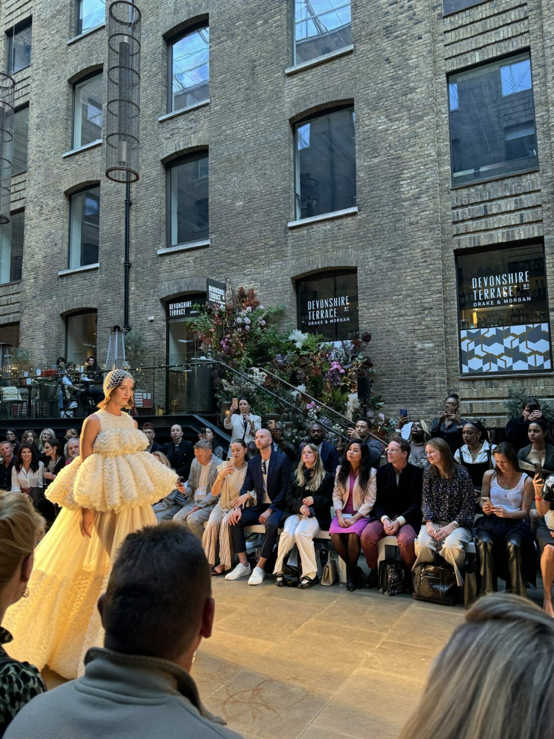 A close up of a model walking on a runway surrounded by people sitting and watching