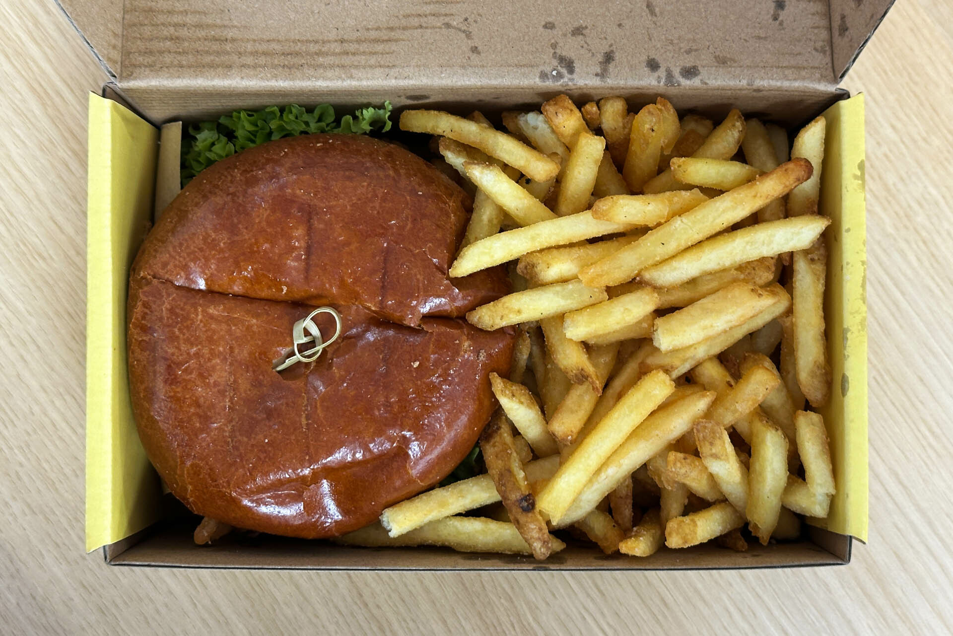 A top shot of the top of a burger with lettuce coming out and a large portion of chips in a box.