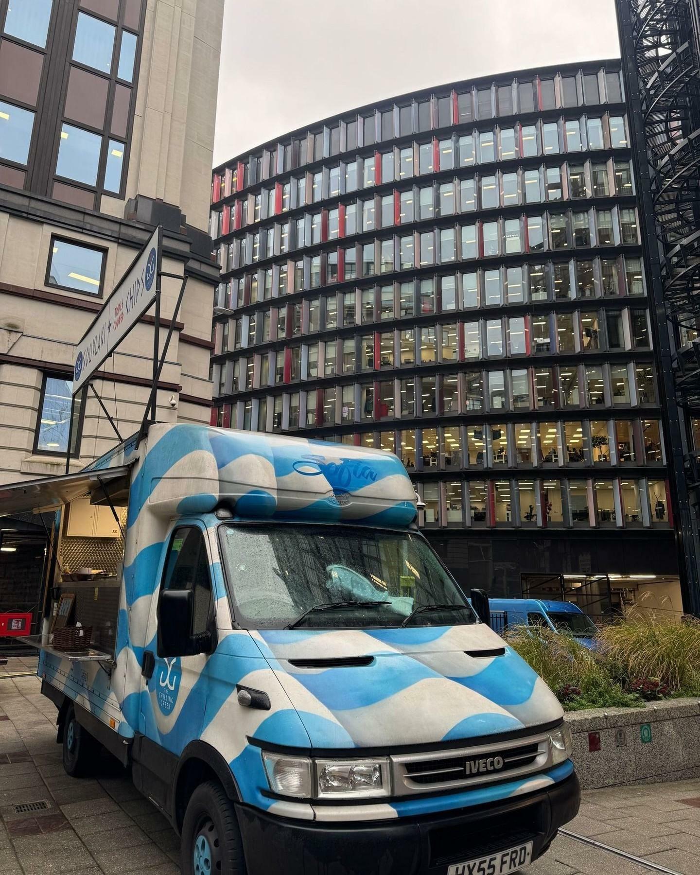 Image of a blue food truck infront of a large glass building