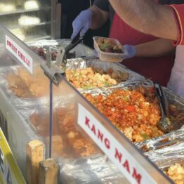 A worker behind a counter filling a box with various Asian foods