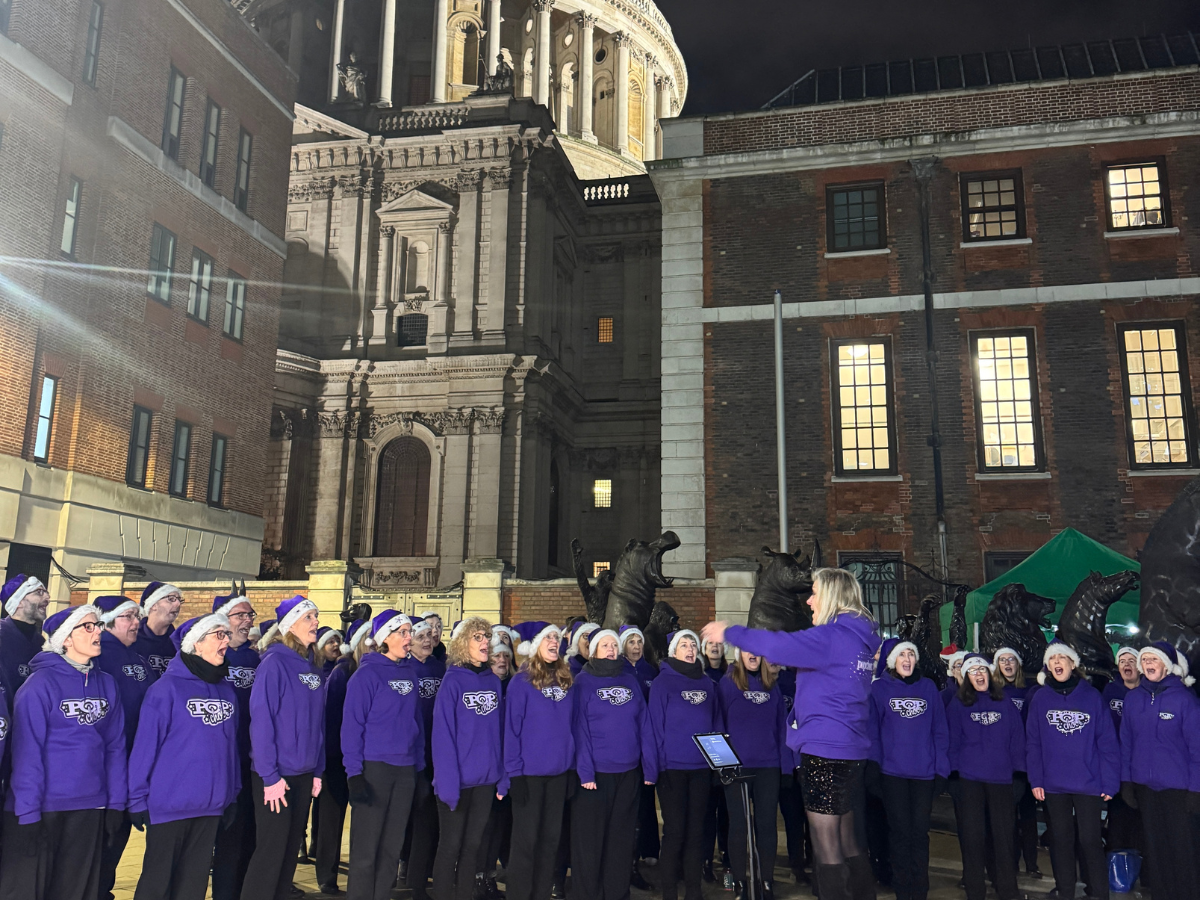 An image of a choir in santa hats standing infront of a conductor with St Paul's in the background.